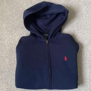 Ralph Lauren Hoodie - Snygg marinblå hoodie från Polo Ralph Lauren med dragkedja och huva. Den är i bra skick utan stora tecken på användning, storleken är barn XL och passar som vuxen S/XS. Skriv gärna vid minsta lilla fråga och såklart kan priset diskuteras!