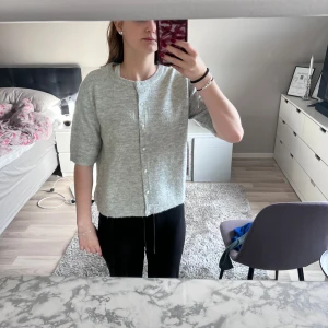 Ljusgrå stickad kofta med pärlknappar - Superfin ljusgrå stickad kofta med pärlknappar och halvlånga ärmar. Koftan har en klassisk rund halsringning och är perfekt att slänga över en topp. Mjuk och skön, passar till många olika outfits.