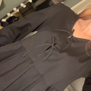 Svart långärmad blus med snörning - Svart blus med långa ärmar och snygg snörning framtill vid halsen. Modellen har en lätt rynkad midja och faller fint. Tyget är tunt och känns luftigt, perfekt för dig som gillar en stilren look med lite edge.