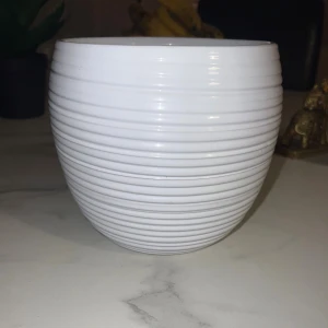 Fin stor kruka - Bilderna visar en vit, glaserad kruka med räfflad yta och en diameter på cirka 15 cm. Krukan är i gott skick utan synliga sprickor eller större skador. Passar utmärkt för inomhusväxter och har en modern, stilren design.