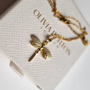Guldfärgat halsband - Supersnyggt halsband med ett guldfärgat trollsländehänge. Vingarna är dekorerade med små glittrande stenar som ger extra bling. Kedjan är tunn och elegant, perfekt för att lyfta vilken outfit som helst. Lådan ingår ej.