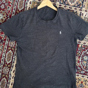 T-shirt från Ralph Lauren - En fin svart/grå polo tshirt. Trycket vid nacken har gått lite bort (se bild). Annars en väldigt fin som kan användas under vardagen.   Undrar du över något eller vill ha fler bilder, tveka inte att kontakta!