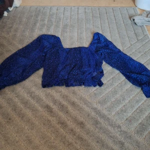 Blå leopardmönstrad blus Amelie & Me - Säljer en blå blus från Amelie & Me i storlek L med leopardmönster. Blusen har långärmade puffärmar och en croppad passform med resår vid midjan. Materialet är lätt och luftigt, perfekt för att sticka ut med coola vibes. Passar för mindre
