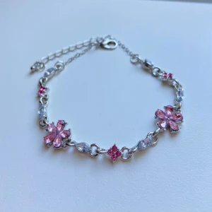 Söt armband med rosa blommor - Armband i silver med rosa detaljer. Kedjan är tunn och justerbar med ett klassiskt lås. Perfekt för dig som gillar söta detaljer och blommiga smycken.