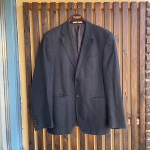 Svart kavaj från 4YOU i linne - Stilren svart kavaj från 4YOU i linne. Klassisk modell med två knappar framtill, tre fickor och snyggt foder. Perfekt för dig som gillar en enkel och tidlös look. Passar till skjorta eller t-shirt för en clean stil.