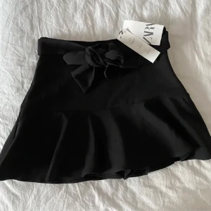 Svart Zara kjol - Kjol med inbyggd shorts under. Hög midja. Knytning i midjan. Knäppning i sidan med dold dragkedja i sömmen. 