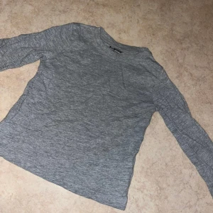 Grå långärmad tröja från Lupilu - En basic grå långärmad tröja från Lupilu i mjuk bomull. Tröjan har rund halsringning och en enkel, rak passform som funkar till allt. Perfekt för lager-på-lager under kyligare dagar.