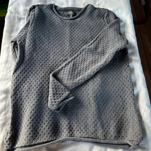 Grå stickad tröja från Newhouse - Mysig grå stickad tröja från Newhouse i 100% bomull. Tröjan har ett diskret strukturmönster, rund halsringning och långa ärmar. 