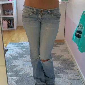 Ljusblå slitna lågmidjade jeans från only - Ljusblå jeans från only med slitningar och hål på knät för en cool, avslappnad look. Klassisk femficksmodell. Bootcut och låg midja. Midja 37 innerben 78. Lite slitna i grenen samt längst ner på jeansen men annars fint skick.