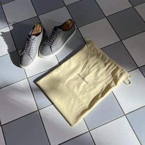 Grå sneakers från Axel Arigato - Snygga grå sneakers från Axel Arigato i skinn med vita sulor och matchande grå snörning. Stilren design med diskret guldfärgad logga på sidan. Skorna har rund tå och platt sula, perfekta för en clean och modern look. Medföljer original dustbag.