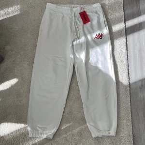Vita mjukisbyxor från Hugo med tryck - Snygga vita mjukisbyxor från Hugo med elastisk midja och snörning. Byxorna har rött Hugo-tryck på benet och broderad logga framtill. Tillverkade i mjuk bomull och har resår vid bensluten samt fickor på sidorna och bak. 