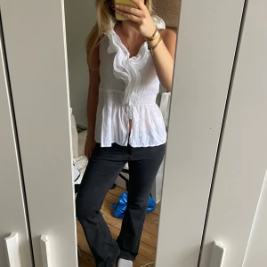 Vit blus med volang från New Look - Säljer en vit blus från New Look med snygga volangdetaljer längs halsen och knäppning framtill. Blusen är ärmlös och har smockad midja som ger en fin form. Materialet är lätt och luftigt, och storleken sitter perfekt på mig med storlek S.💗