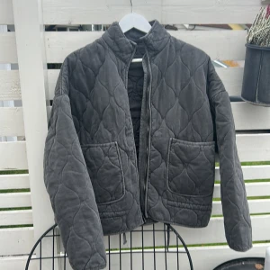 Grå quiltad jacka med dragkedja - Quiltad jacka i mörkgrå färg med snyggt mönster och två stora fickor framtill. Jackan har hög krage, dragkedja och är helfodrad. Perfekt för kyliga dagar och ger en cool vibe till din outfit. Helt oanvänd! Fick hem den idag men passade ej. Så säljer den vidare till någon annan! Vid snabb affär kan den säljas för 500kr!