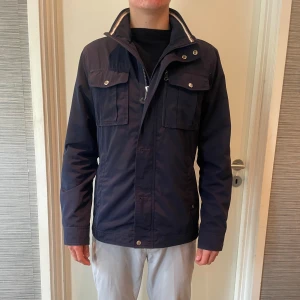 Fieldjacket J.Lindeberg  - Säljer en jättefin fieldjacka ifrån J.Lindeberg i storlek medium, passar även small. jättefint skick dock en liten defekt på ryggen som syns på bilden men inget som syns vid användning. Hör gärna av dig om du har några frågor