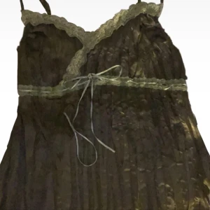 Brun omlotttopp med spetsdetaljer - Supersöt  olivgrön  topp med tunna axelband, omlott över bysten och fina  ljusgröna spetsdetaljer längs kanterna, även räfflig under byst/har volanger