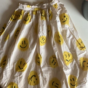 Maxi kjol från Molo med smileys - Maxi kjol från Molo i beige med gula/svarta emojis i storlek 134/140. 100 procent bomull.