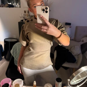 Beige blus med knyt och knappar - Säljer en beige blus med markerad midja och knytband i ryggen. Blusen har puffiga trekvartsärmar och coola svarta knappar på axeln. Från zara i storlek S💛🧡