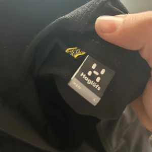Svart vindjacka från Haglöfs, stl L - Säljer en svart vindjacka från Haglöfs i storlek L. Jackan har minimalistisk design med dragkedja framtill och diskret Haglöfs-logga på bröstet. Perfekt för dig som gillar stilren och funktionell ytterjacka. Långärmad och lätt material.
