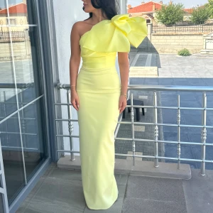 Ljusgul långklänning med stor rosett - Supersnygg ljusgul långklänning med en axel och en stor dramatisk rosett på axeln. Klänningen har figurnära passform och är tillverkad i ett slätt, elegant material. Perfekt för dig som vill sticka ut och känna dig extra glam. Nypris 2000kr 