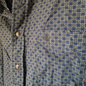 Blommig - Skogs-grön skjorta med små blå och gröna blommor. (Säljer åt min partner). I vanligt, lite styvare skjorttyg, och snygg när den är struken eller varit upphängd (istället för nedkastad i en låda 😅)