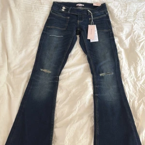 Bootcut jeans från Gina Tricot XS - Mörkblå flare low waist jeans från Gina Tricot i storlek XS 14+. Jeansen har slitna detaljer på låren, klassiska fickor och dubbla knappar i midjan.  Perfekta för dig som gillar en trendig och avslappnad stil. 