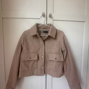 Beige kappa från Zara i ullmix - Snygg beige kappa från Zara i ullmix med stora fickor framtill och knappar i guld färgad metall. Jackan är croppad och har klassisk krage samt långa ärmar. Perfekt för lager-på-lager dagar eller samt varmare höst dagar som ger en clean look. Använd 2 gånger så skicket är som nytt! Ny pris 550 kr men säljer för 300 pris kan diskuteras!🩷