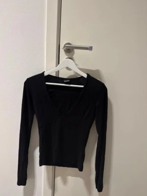 Svart långärmad v-ringad topp - Säljer en svart långärmad topp med djup v-ringning och figurnära passform från Gina Tricot. Toppen är stretchig!  Använd en gång 