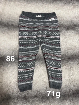 Mönstrade stickade byxor Newbie - Mysiga stickade byxor från Newbie i grått. Byxorna har ett klassiskt vintermönster och mjuk resår i midjan och benslut. Perfekta för kalla dagar och riktigt sköna att ha på sig.🌸 Fint använt skick. Storlek 86