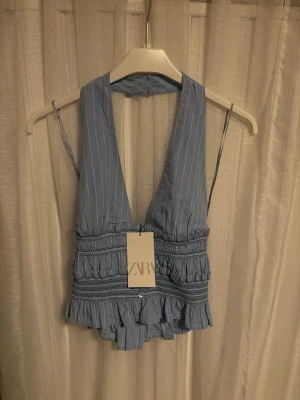 Blå randig halterneck top från Zara - Supersöt blå halterneck top från Zara med tunna vita ränder, djup v-ringning och bred krage som knäpps i nacken med. Det är storlek S och är helt oanvänd med prislappen kvar.🩵