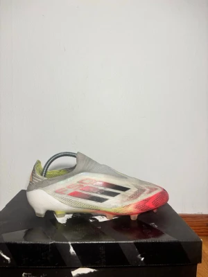 Adidas F50 fotbollsskor röd/vit - Säljer ett par Adidas F50 fotbollsskor med en clean design i vitt, rött och inslag av svart och gult. Skorna har platt sula med dobbar och är tillverkade i syntetmaterial för lätt känsla på planen. Perfekt för dig som vill ha speed och kontroll under matchen.