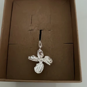 Silverfärgat blom-halsband från Pilgrim - Snyggt halsband från Pilgrim i silverfärg med ett stort, blommigt hänge i organisk form. Kedjan är tunn och elegant med ett mindre blomformat hänge vid låset. Perfekt accessoar för att lyfta din outfit med en unik touch.