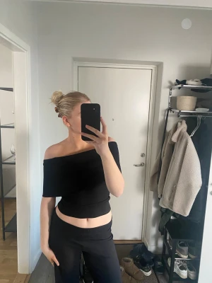 Svart offshoulder topp från Zara - Säljer en svart offshoulder topp från Zara i storlek M. Toppen har en croppad passform och är ärmlös med smala axelband. Materialet är mjukt och stretchigt, perfekt för en trendig look. Enkel att styla med både jeans och kjol.