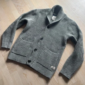 Grå stickad kofta  - Säljer en grå stickad kofta med krage och stora knappar framtill. Storlek L men passar M. Skitsnygg med en skjorta under! Perfekt för lager-på-lager och chill vårstil. Har du en fråga? Hör av dig! 