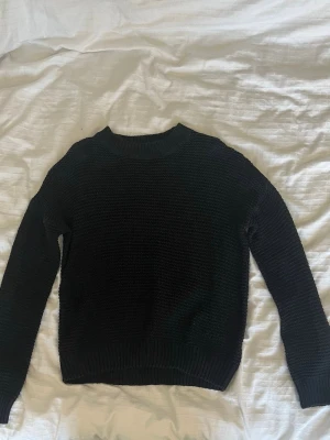 Svart stickad tröja - Mysig svart stickad tröja från 157 i storlek M. Tröjan har en klassisk rund halsringning och ribbade muddar vid ärmslut och nederkant. Perfekt för kyliga dagar och enkel att matcha med allt.