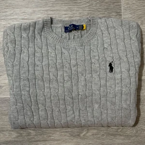 Grå kabelstickad tröja Polo Ralph Lauren - Grå kabelstickad tröja från Polo Ralph Lauren med rund hals, broderad logga och ribbade muddar. Långärmad, stilren och tidlös. Storlek M (passar även S). Pris kan sänkas vid snabb affär 🤩