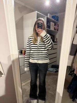 Randig kofta från Gina Tricot - Säljer en stickad kofta från Gina Tricot i vitt och svart med horisontella ränder. Koftan har guldiga knappar framtill, två små fickor och lång ärm. 