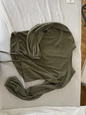 Olivgrön ribbad topp från BikBok - Säljer en olivgrön långärmad topp från BikBok i ribbad stretchig polyester. Toppen har rund hals, med knyt i midjan och en croppad passform. Perfekt till jeans eller kjol för en chill look.