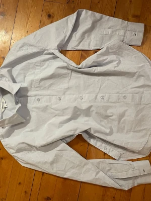 Ljusblå skjorta från Kappahl - Klassisk ljusblå skjorta från Kappahl i bomull. Skjortan har lång ärm och knappar framtill & på sidan. Perfekt till jeans för en clean look.