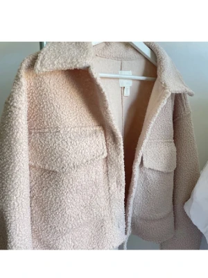 Beige teddyjacka med stora fickor - Supermjuk och fluffig teddyjacka i beige från H&M. Jackan har stora bröstfickor med lock, klassisk krage och knäppning med stora knappar framtill. Perfekt croppad längd och loose fit för en chill vibe.