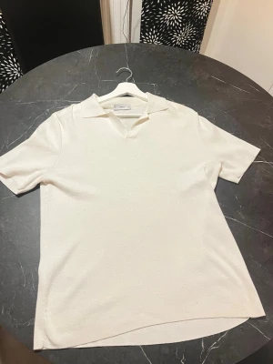 Vit piké t-shirt från Mango - Säljer en stilren vit piké t-shirt från Mango med krage och v-ringad hals. T-shirten har korta ärmar och är gjord i ett mjukt bomullsmaterial. Perfekt för dig som gillar en clean och enkel look. Dessutom från Gibraltar.