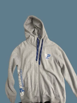 Grå zip-hoodie med blå detaljer – Proficient - Grå hoodie med dragkedja och huva från Proficient. Snygga blå detaljer och tryck på bröstet samt längs sidan. Mjuk och bekväm modell, perfekt för vardag eller träning. Använd men i bra skick, inga kända defekter. Unisexmodell.