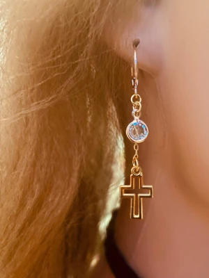 By prisförslag- 1 st Guldig örhänge med kors och sten - 1 snyggt örhänge i guld-look med ett hängande kors och en liten glittrande sten ovanför. Örhänget har en tunn, elegant form och passar perfekt för dig som gillar detaljer med lite edge. Perfekt accessoar för att lyfta din stil.