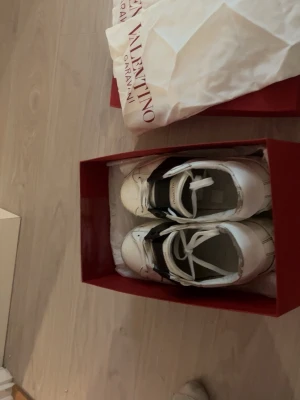 Valentino Garavani Open sneakers - Säljer ett par vita Valentino Garavani Open sneakers köpta i NK med bred svart läderdetalj över vristen. Klassisk låg modell med snörning och rund tå. Skorna är i skinn och har diskret Valentino-logga på plösen. Kommer med originalkartong och dustbag. såldes för dem blev för små