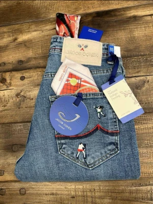 Jacob Cohën ljusblå jeans med brodyr - Unika ljusblå jeans från Jacob Cohën med broderade figurer på bakfickan och röda kontrastsömmar. Klassisk femficksmodell i mjuk bomullsdenim, detaljer som broderad logga och exklusiva etiketter. Perfekt för dig som vill sticka ut med stil.