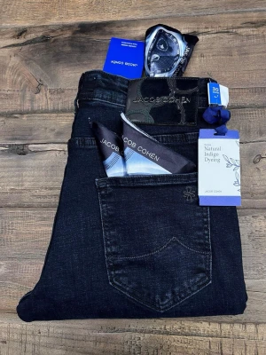 Mörkblå jeans från Jacob Cohën - Säljer ett par mörkblå jeans från Jacob Cohën med snygga detaljer och naturlig indigofärgning. Jeansen har klassisk femficksdesign, exklusiv patch bak och coolt mönstrat innerfoder. Materialet är mjukt och stretchigt för extra komfort.
