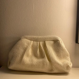 Vit clutch - Säljer en stilren vit clutch. Väskan har en rymlig insida och stängs med en elegant ram. Perfekt för att ge en chic touch till din outfit.