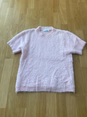Ljusrosa fluffig kortärmad tröja - Supersöt ljusrosa fluffig tröja från med korta ärmar och rund hals från blue vanilla. Perfekt för dig som gillar mjuka material och vill ha en mysig men ändå stylish look. Passar till både jeans och kjol.