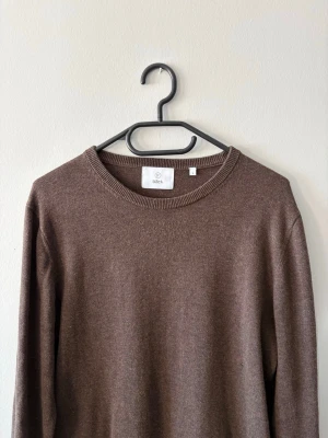 Brun stickad tröja från Bläck - Mysig brun stickad tröja från Bläck i storlek S. Klassisk rund halsringning och långa ärmar. Perfekt till höst och vinter när du vill ha något enkelt men ändå stilrent. Liten skada vid sidan av magen men inget som syns.