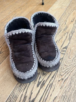 Bruna boots från Mou med stickade detaljer - Mysiga bruna boots från Mou med grå stickade kanter och mjukt foder. Skorna är tillverkade i mocka och har en platt sula. Perfekta för kalla dagar och ger en avslappnad men ändå snygg look.