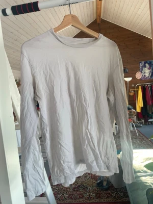 Vit långärmad tröja från H&M - En basic vit långärmad topp från H&M i regular fit. Tillverkad i mjuk bomull med rund halsringning och enkel design, perfekt att styla lager på lager eller bära som den är. 